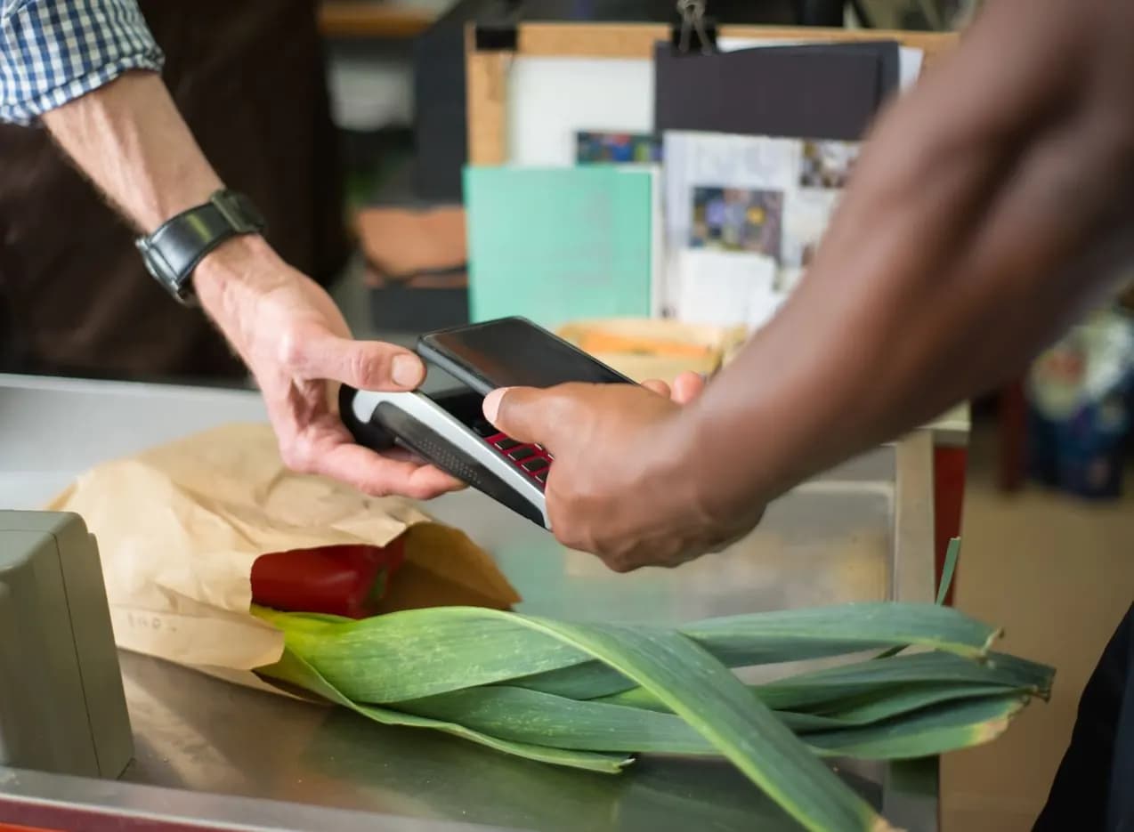 A customer holding a phone to a payment terminal at a shop counter